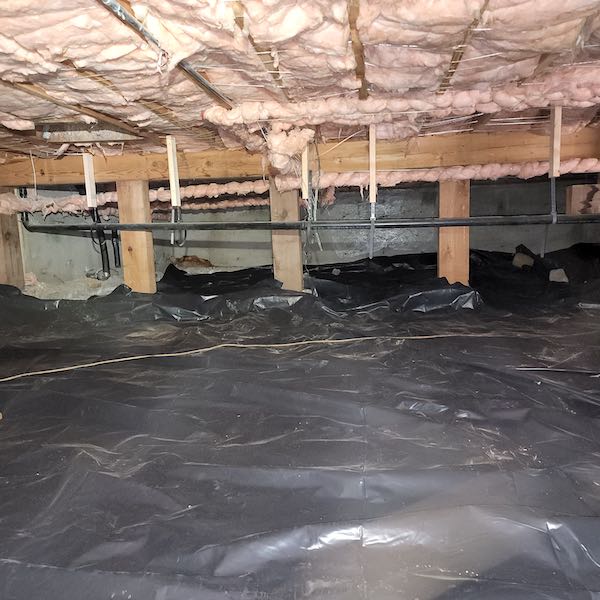 Crawl space under a house with pink insulation above and black pvc membrane below, covering the ground.
